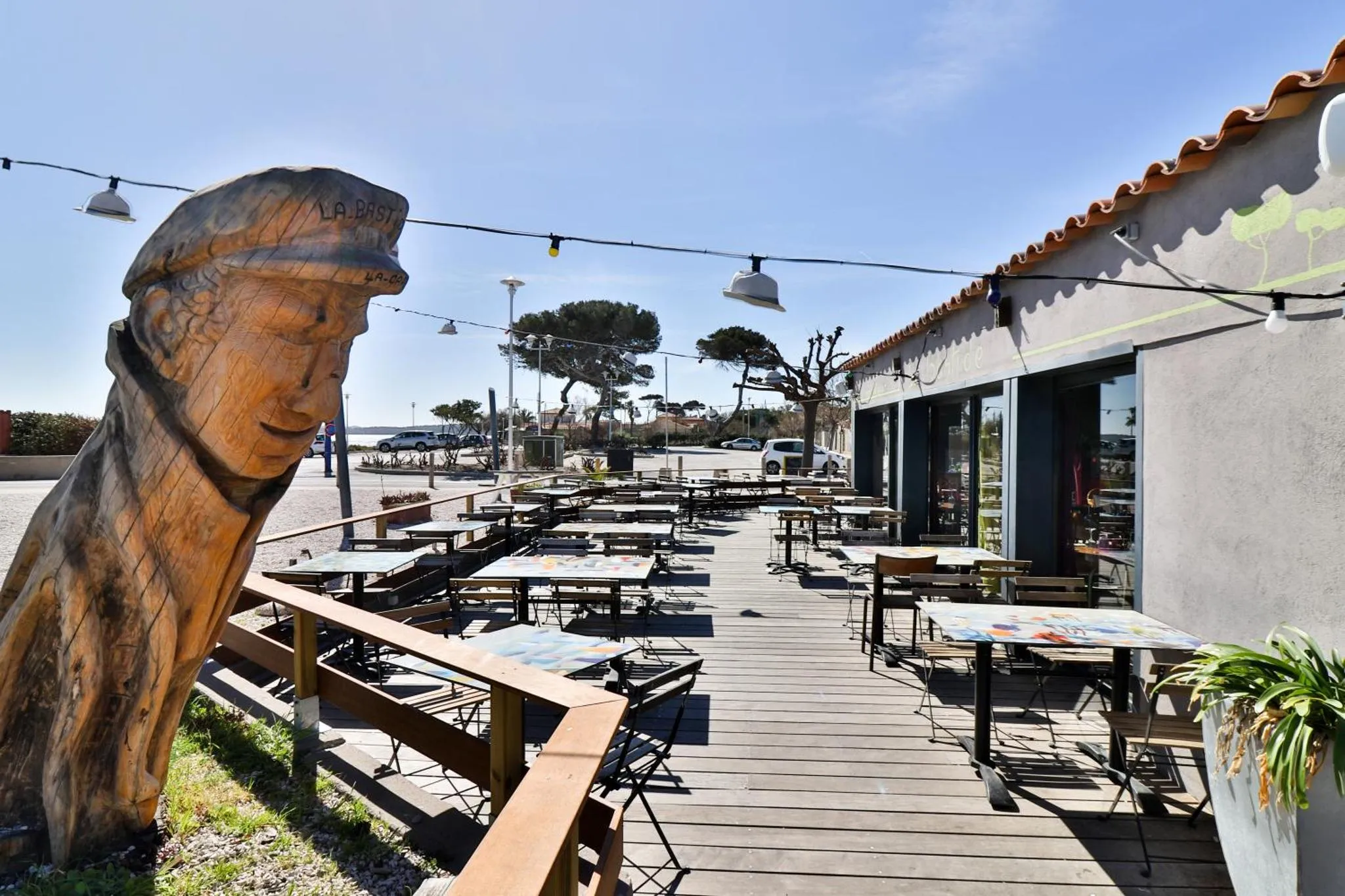 Terrasse ombragée avec tables et chaises en bois près d'un bâtiment.