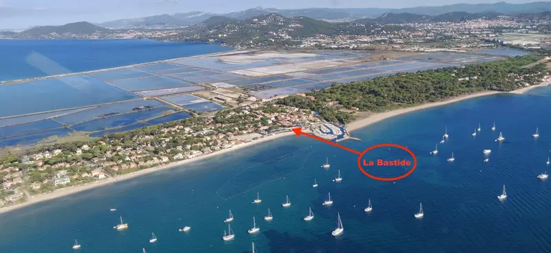 Vue aérienne d'une côte avec une plage, des marais salants et des montagnes en arrière-plan.