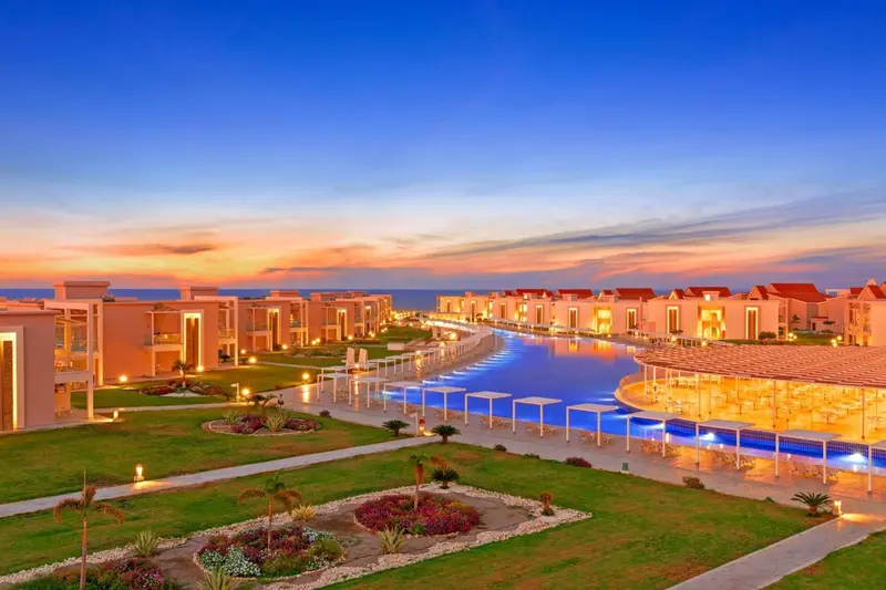 Vue aérienne d'un complexe hôtelier avec piscine et végétation luxuriante au coucher du soleil.