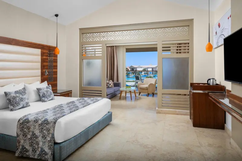 Chambre lumineuse avec un grand lit et une vue sur la mer par de larges baies vitrées.