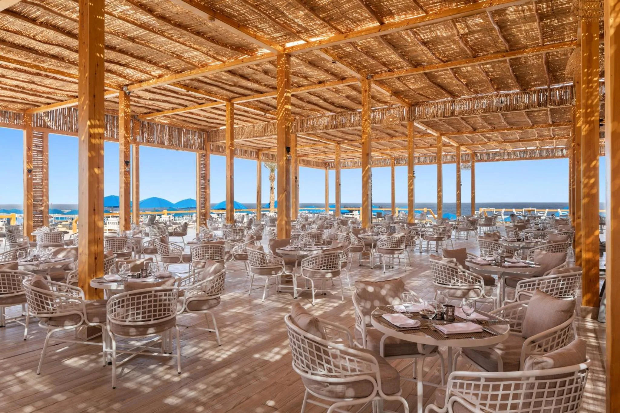 Terrasse ombragée avec tables et chaises donnant sur la mer.