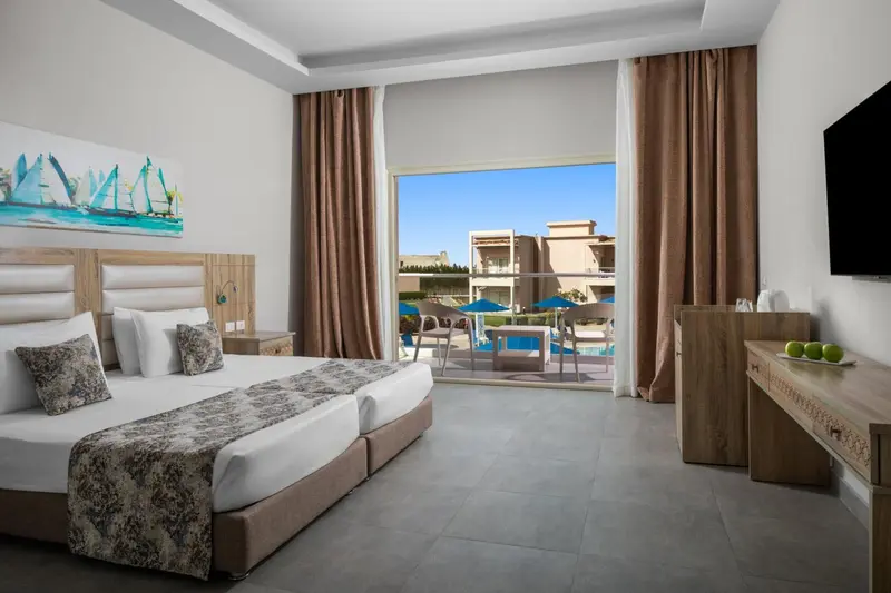 Chambre lumineuse avec un grand lit et vue sur une piscine ensoleillée.