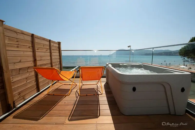 Deux chaises longues orange se trouvent sur une terrasse en bois avec un jacuzzi et une vue sur la mer.
