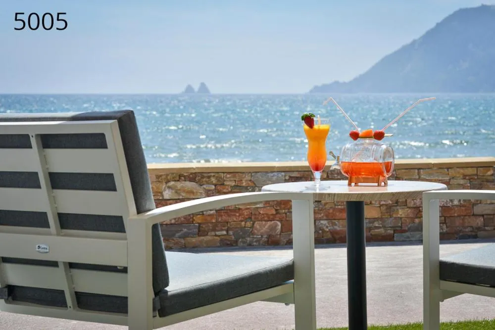 Deux fauteuils de jardin face à la mer avec des boissons colorées sur une petite table.