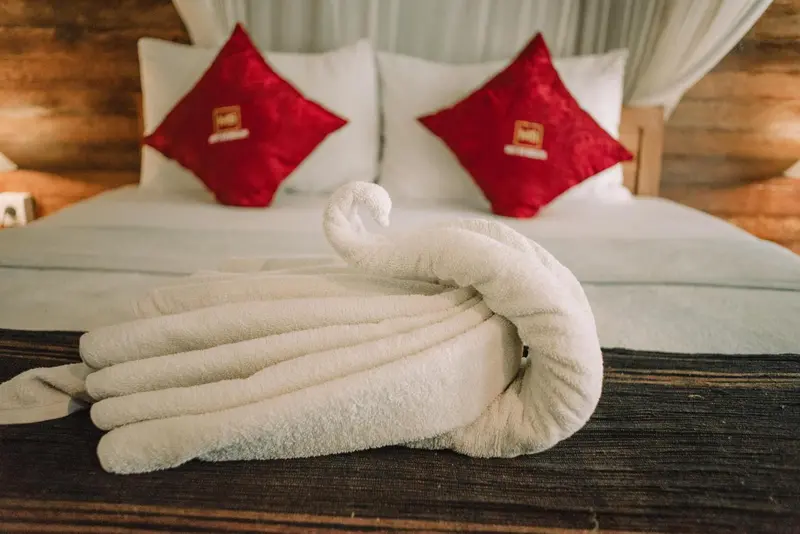 Un lit est soigneusement fait avec des oreillers rouges et une serviette en forme de cygne.