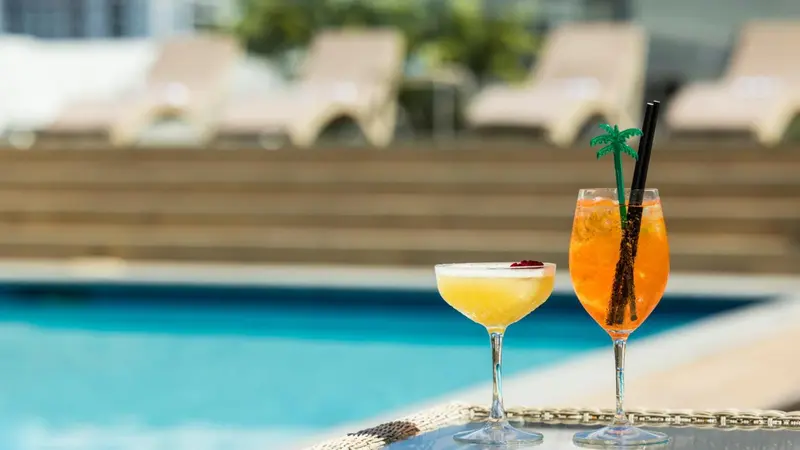 Deux cocktails colorés sur une table basse au bord d'une piscine.
