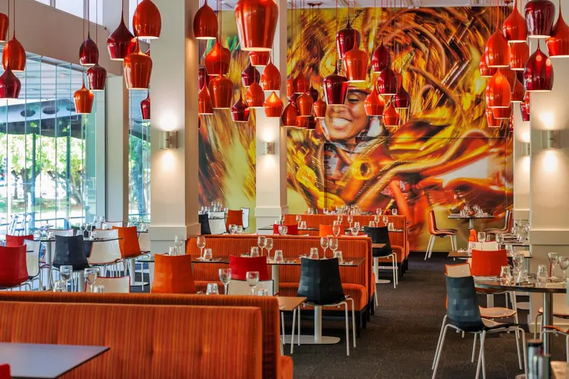 Une salle de restaurant lumineuse avec des banquettes orange et des suspensions décoratives.