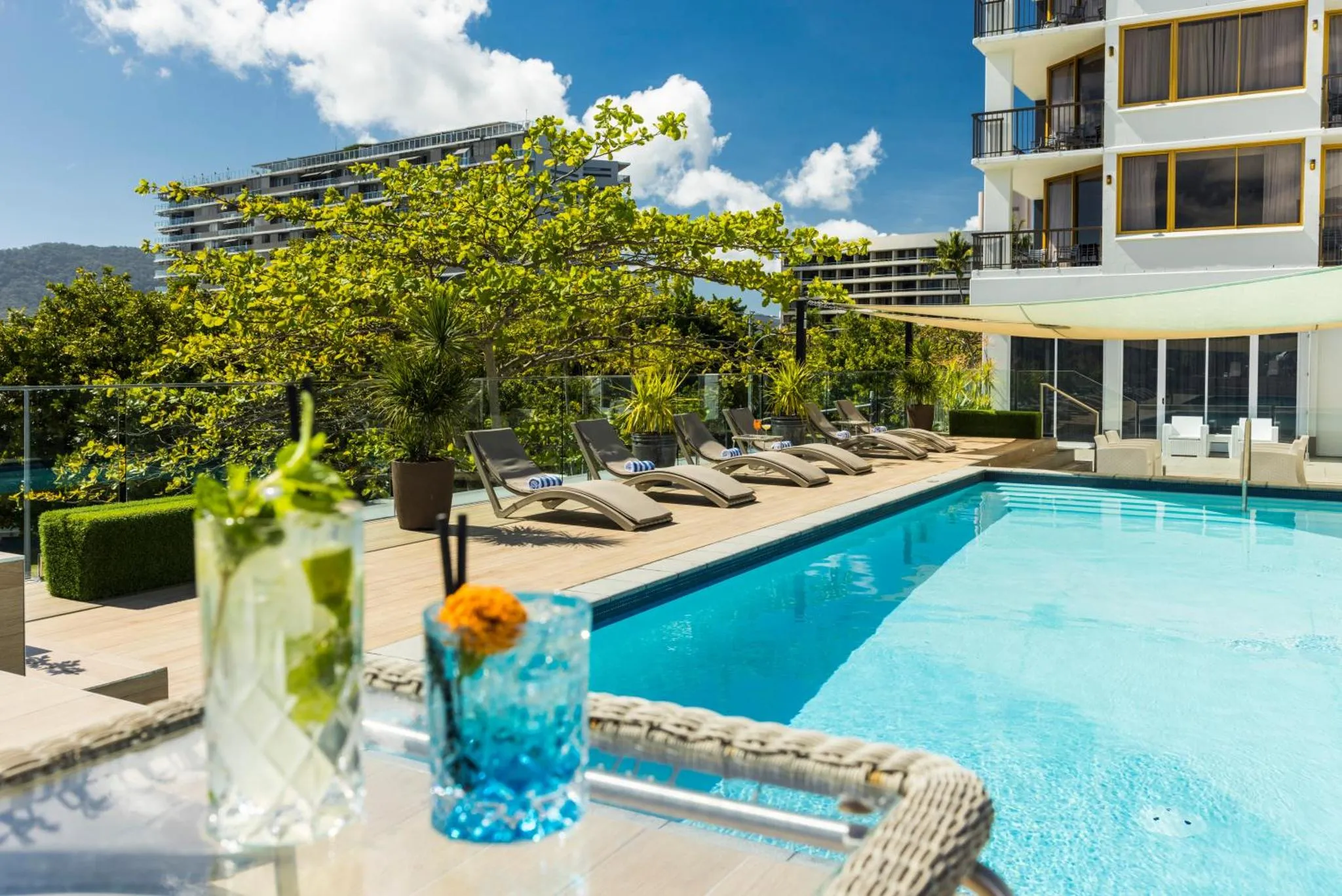 Deux cocktails colorés sur une table basse près d'une piscine ensoleillée.