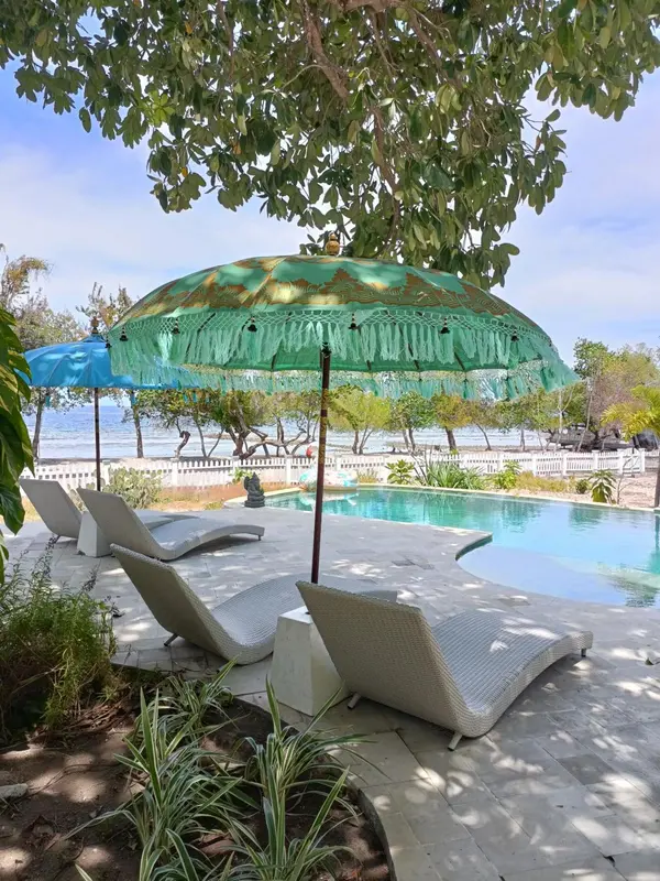 Transats et parasol ombragent une piscine bordée de végétation.