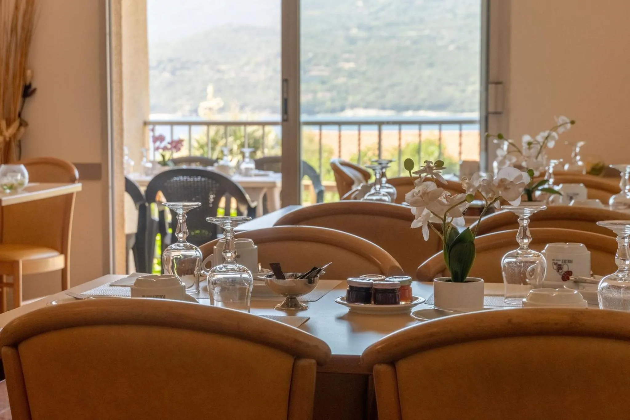Une table est dressée avec de la vaisselle et des fleurs, face à une vue sur la mer.