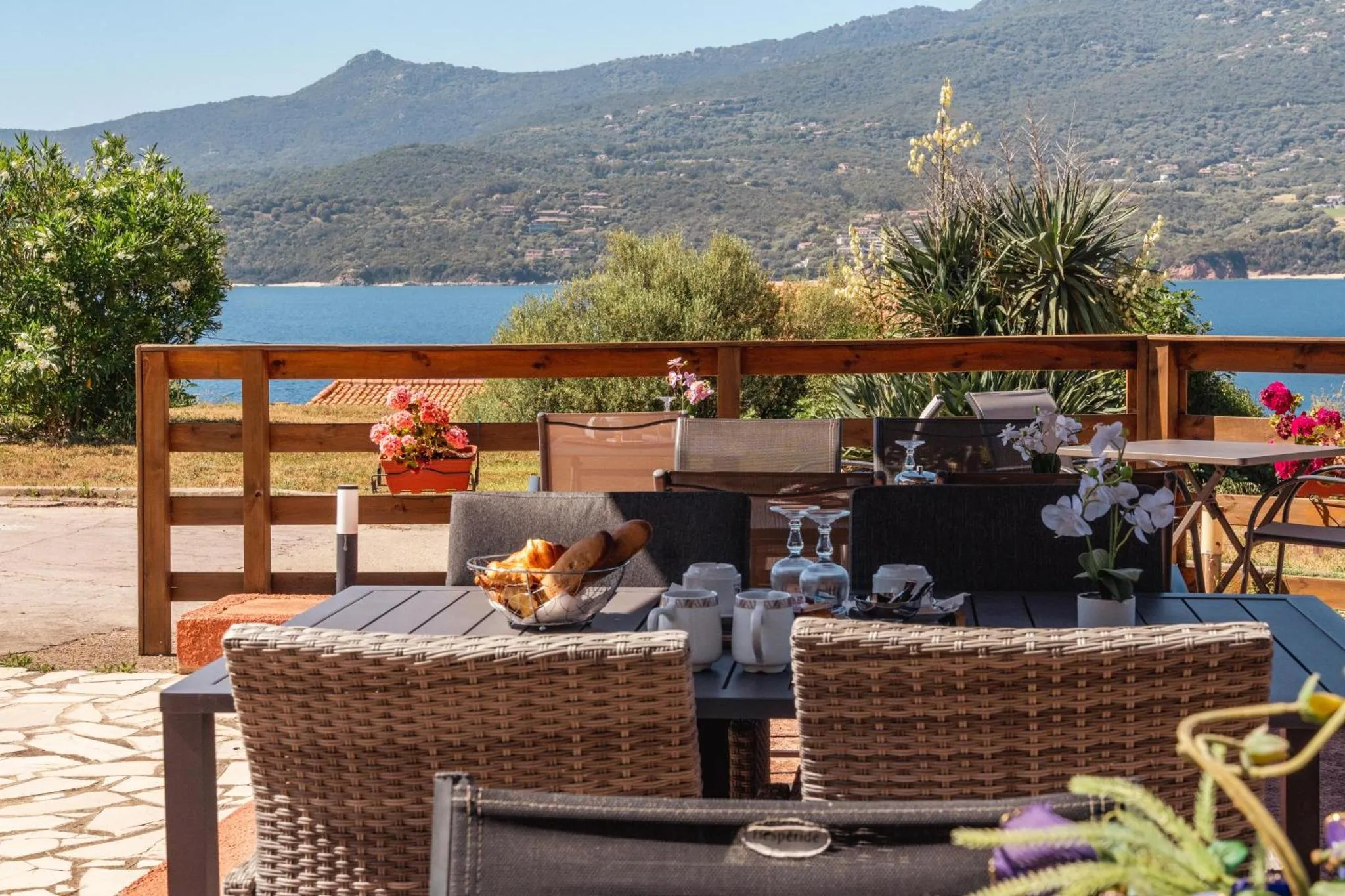 Une table de petit-déjeuner est dressée sur une terrasse avec vue sur la mer et les montagnes.