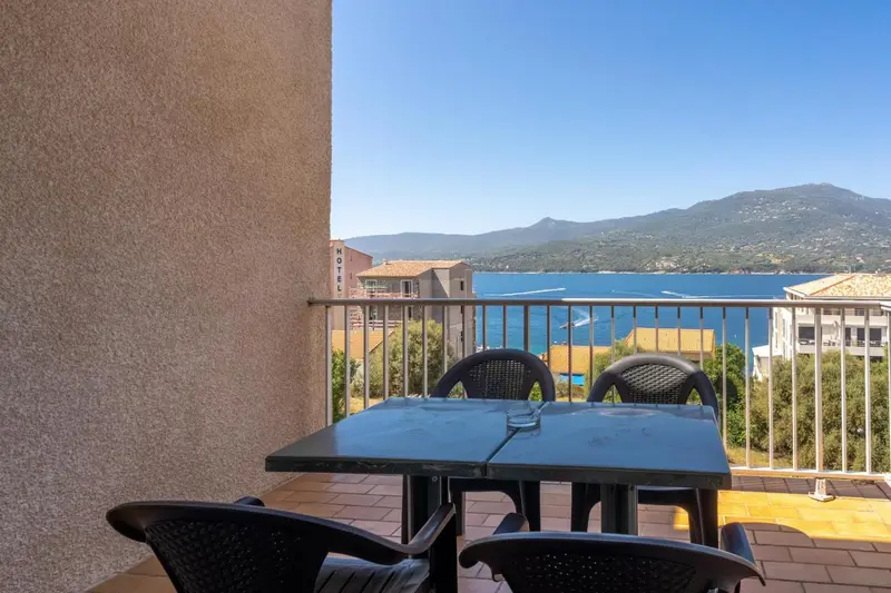 Une terrasse avec une table et des chaises offre une vue sur la mer et les montagnes.