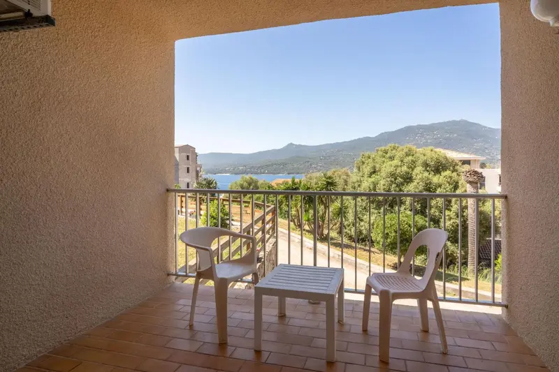 Terrasse avec deux chaises et une petite table donnant sur un paysage montagneux et la mer.