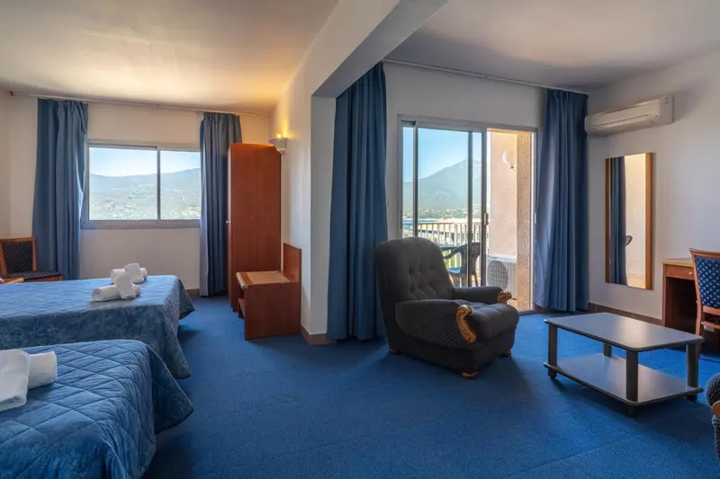 Une chambre d'hôtel lumineuse avec un coin salon et une vue sur la montagne.