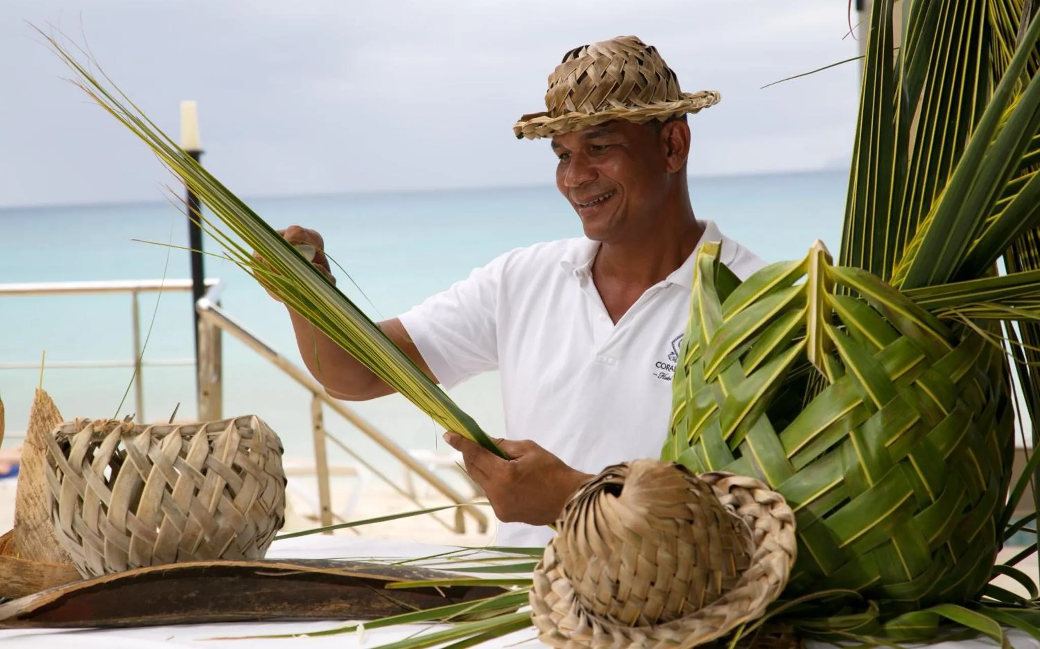 Un homme souriant tisse des feuilles de palmier sur une table en bord de mer.