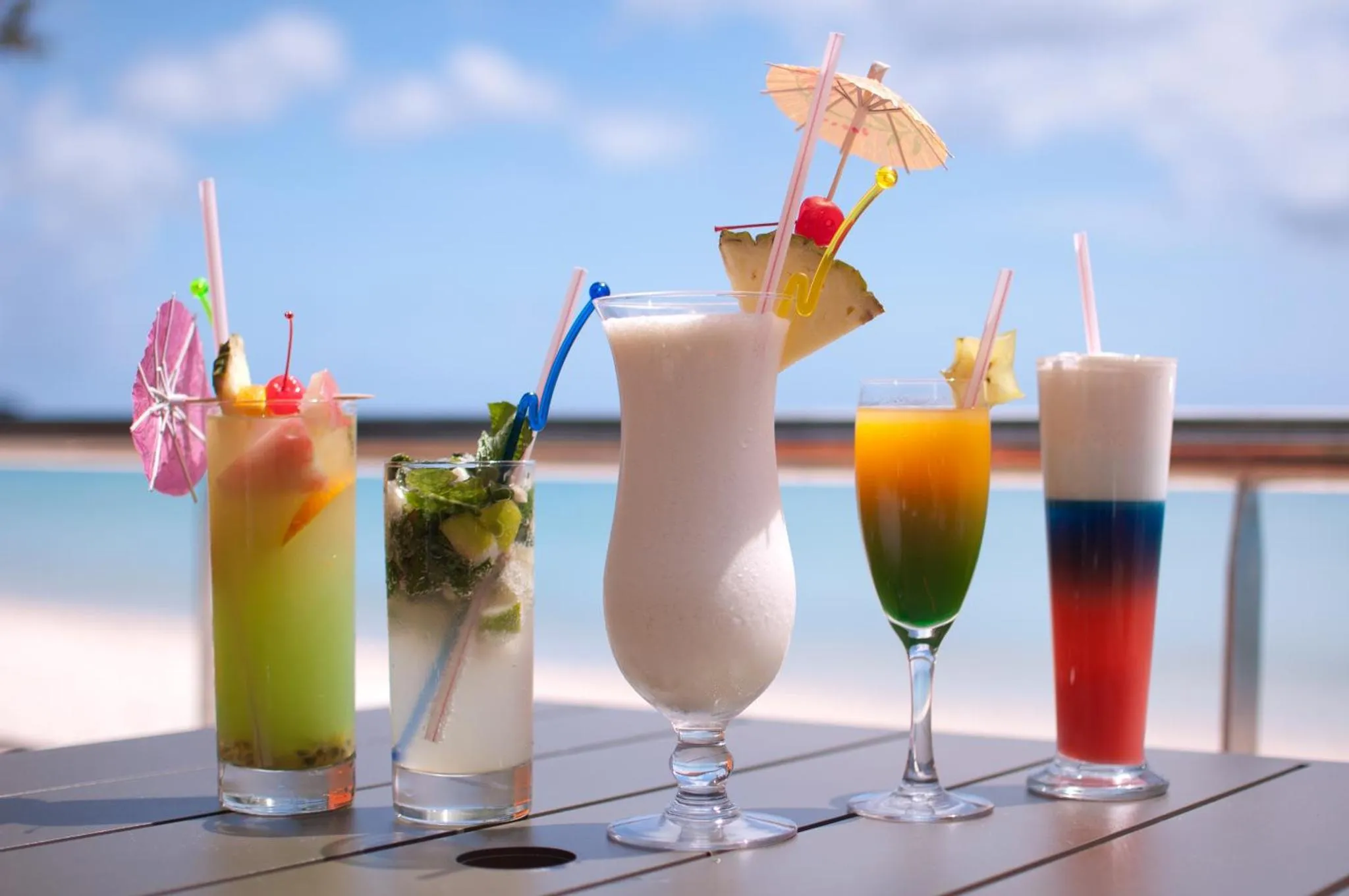 Des boissons colorées sont présentées sur une table en extérieur avec vue sur la mer.