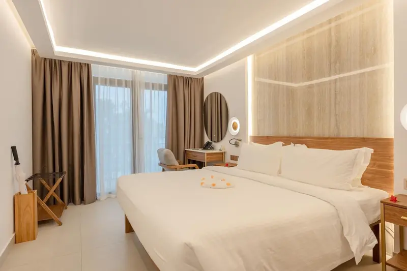 Chambre lumineuse avec un grand lit et un bureau près de la fenêtre.