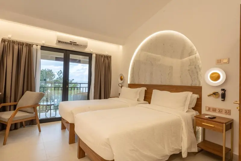 Chambre lumineuse avec deux lits simples et vue sur la végétation.