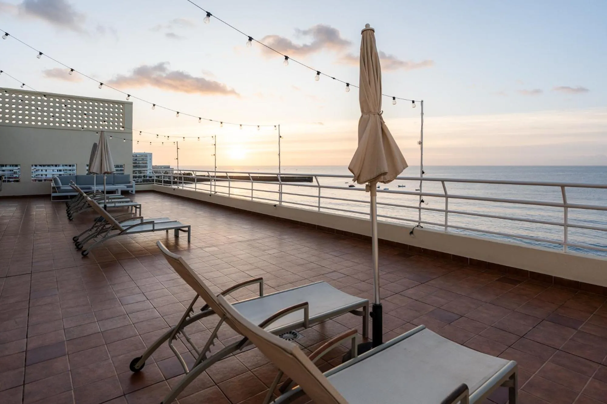 Terrasse avec transats et parasols face à la mer au coucher du soleil.