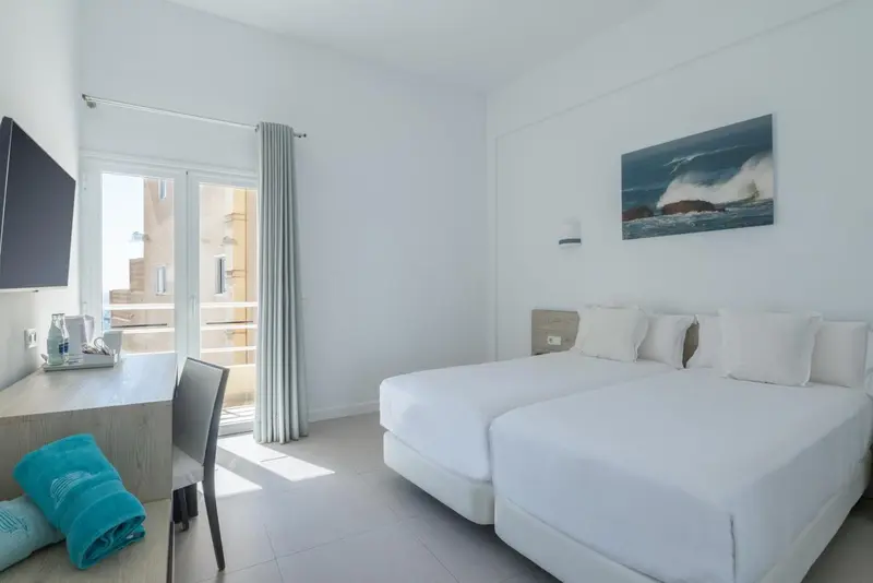 Chambre lumineuse avec lits jumeaux et vue sur l'extérieur.