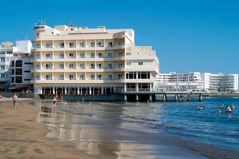 Bâtiment beige avec des balcons donnant sur une plage et la mer.