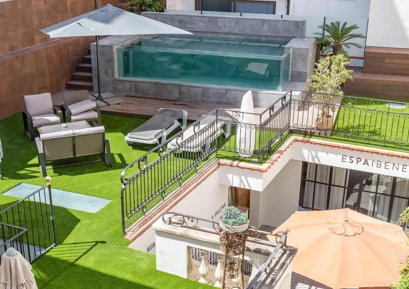 Petite piscine rectangulaire entourée d'une terrasse aménagée avec des transats et de la végétation.