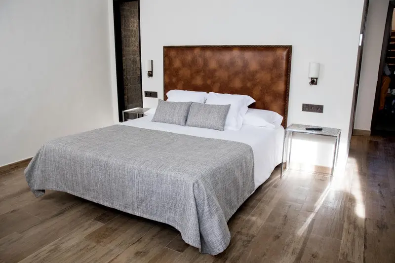 Une chambre lumineuse avec un grand lit recouvert d'une couverture grise.