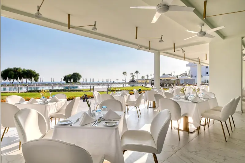 Une salle à manger lumineuse avec des tables dressées face à un paysage côtier.