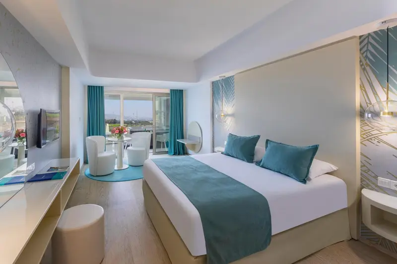 Chambre lumineuse avec un grand lit et un coin salon donnant sur une vue dégagée.