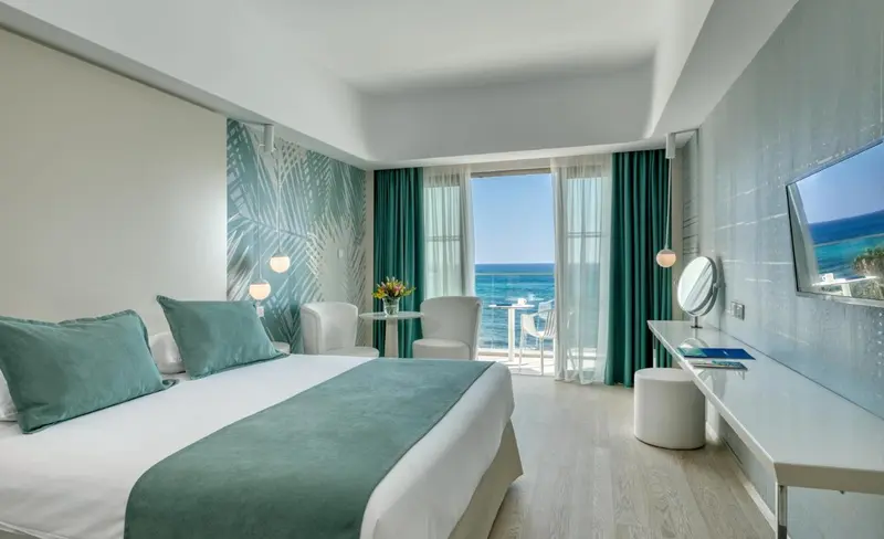 Une chambre lumineuse avec un grand lit et un balcon donnant sur la mer.