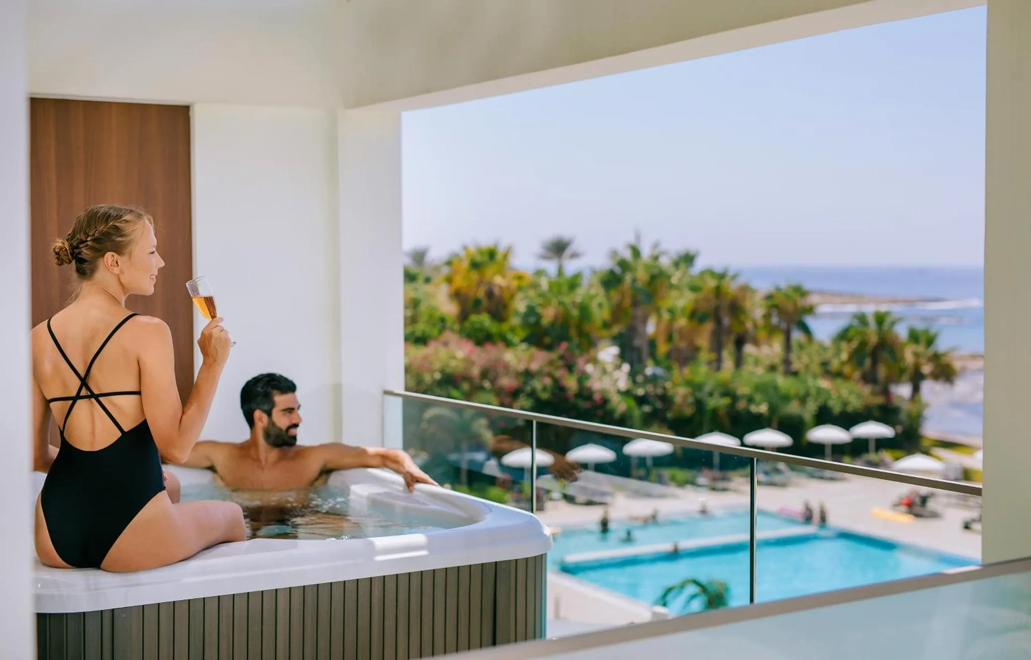 Une femme et un homme se détendent dans un jacuzzi sur une terrasse avec vue sur la mer et une piscine.