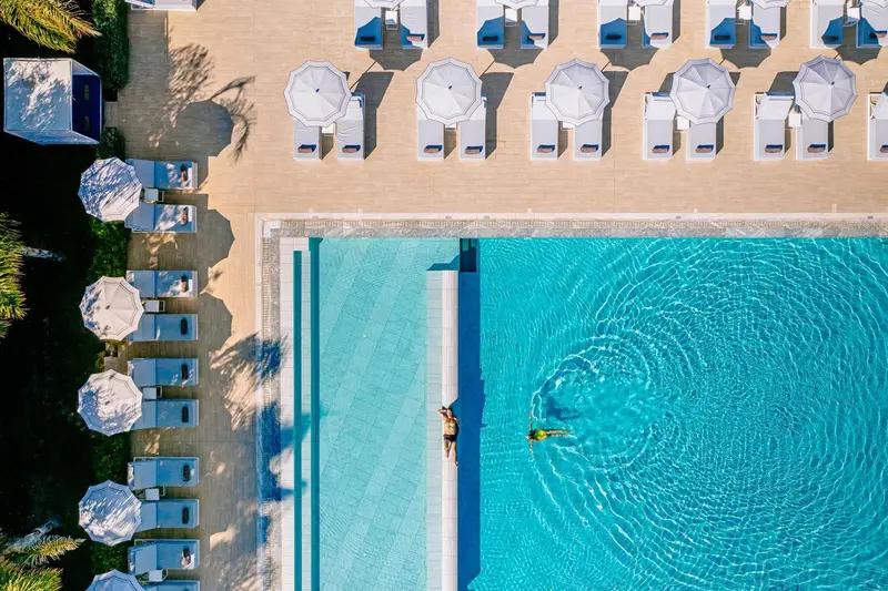Vue aérienne d'une piscine et de transats sous des parasols.