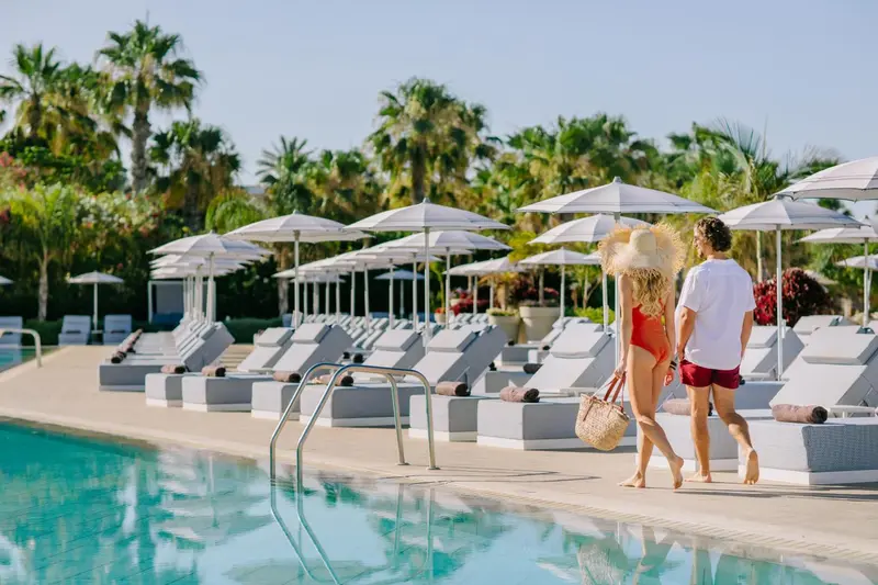 Couple marchant le long d'une piscine bordée de transats sous des parasols.