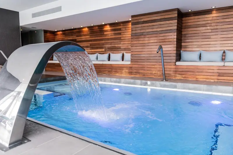 Une cascade d'eau se déverse dans une piscine intérieure aux murs en bois.