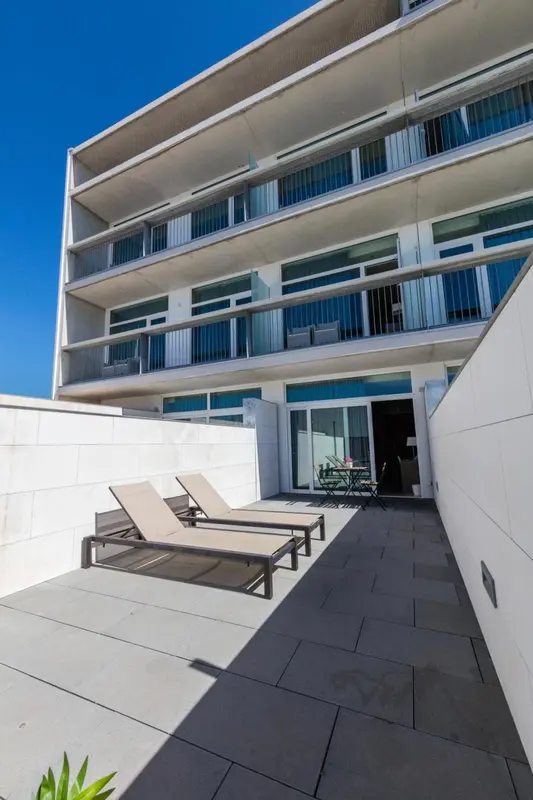 Terrasse ensoleillée avec chaises longues devant un bâtiment moderne.