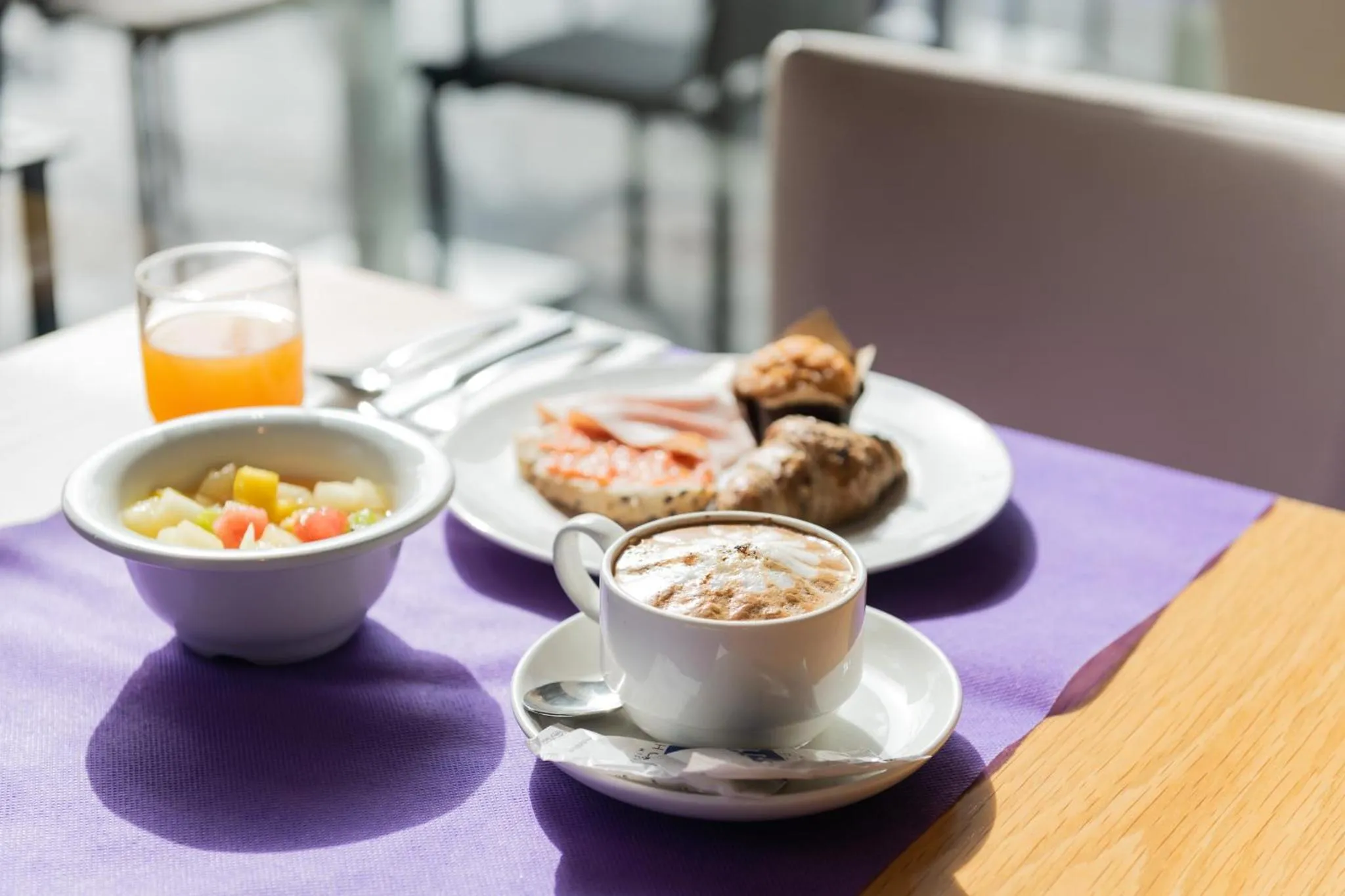 Une table est dressée avec un petit-déjeuner composé de fruits, de viennoiseries et d'une boisson chaude.