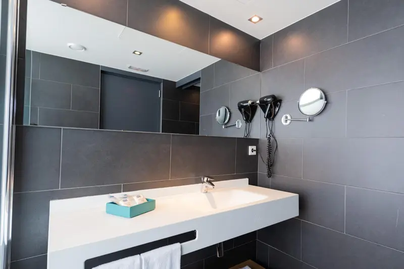 Une salle de bain moderne avec un grand miroir et un lavabo blanc.