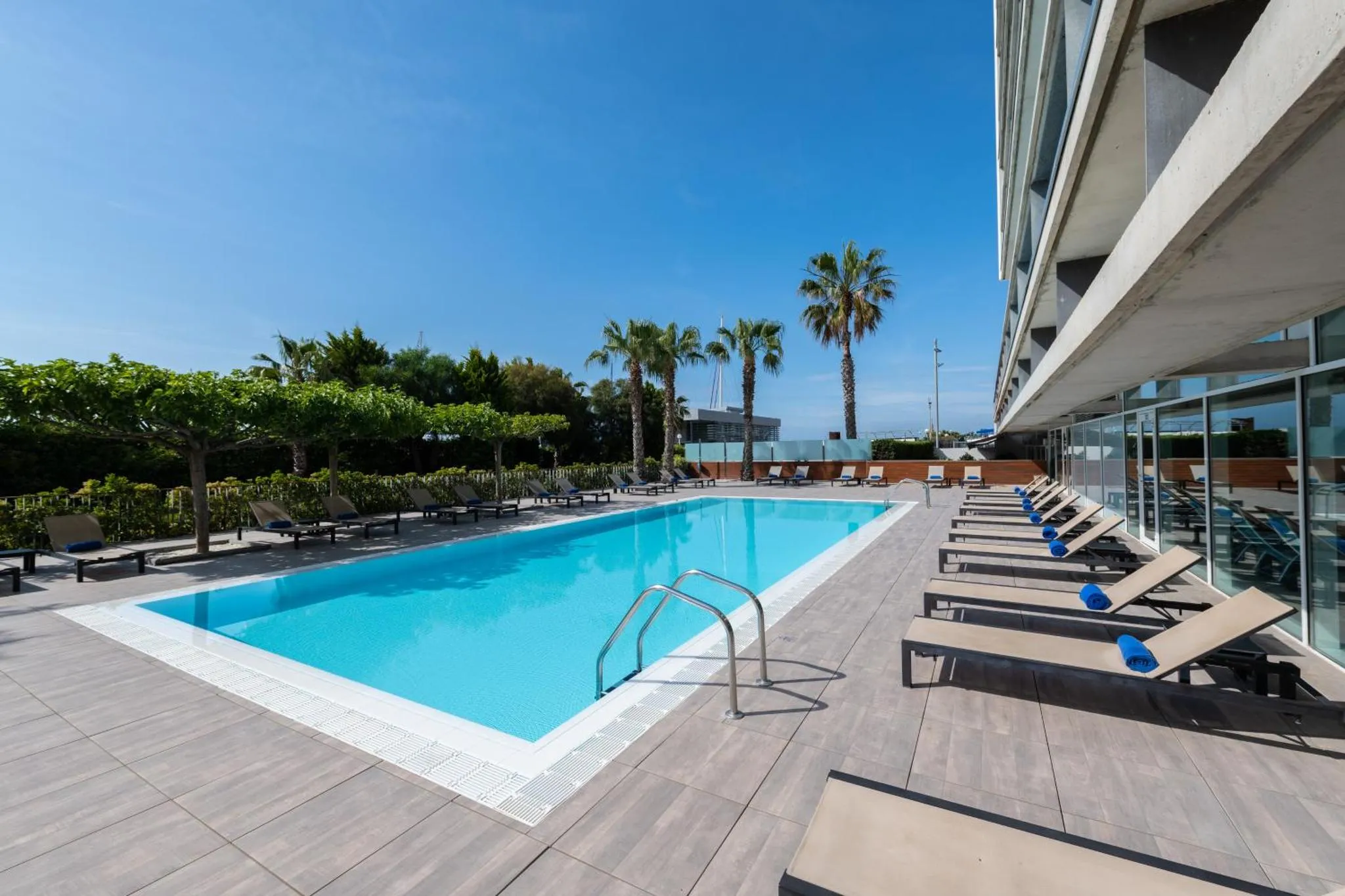 Une piscine rectangulaire bordée de transats sous un ciel bleu.