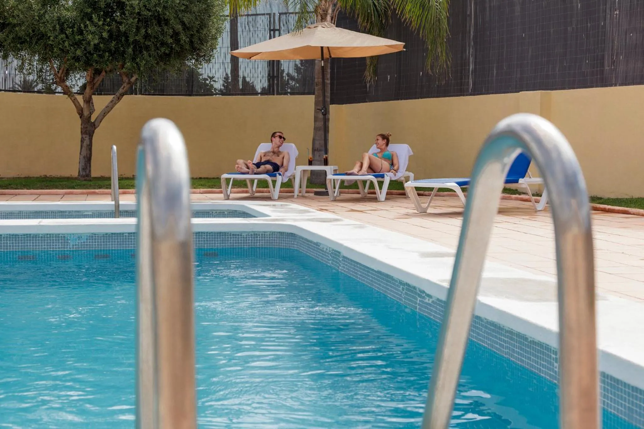Deux personnes se relaxent sur des transats au bord d'une piscine ensoleillée.