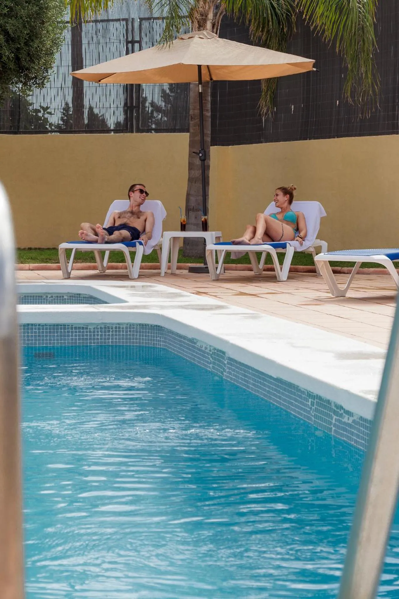 Deux personnes se relaxent sur des transats au bord d'une piscine ensoleillée.