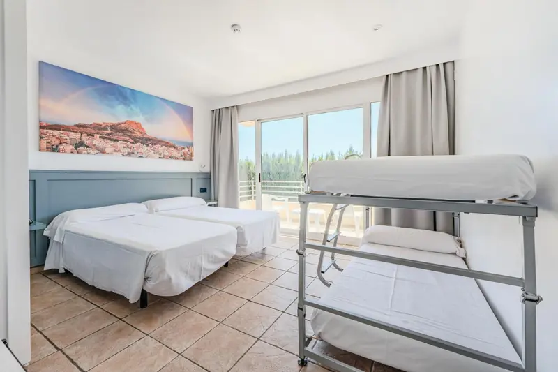 Une chambre lumineuse avec lits jumeaux et un lit superposé près d'une baie vitrée.
