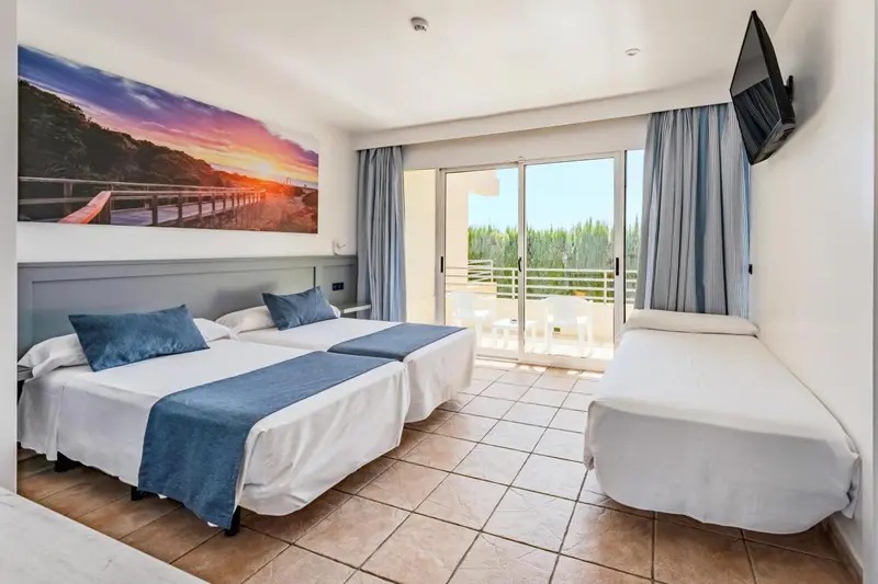 Chambre lumineuse avec deux lits simples et un lit d'appoint, donnant sur une terrasse.