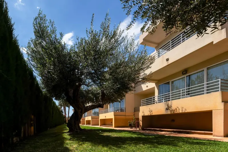 Façade d'un bâtiment beige avec des balcons et un jardin verdoyant.