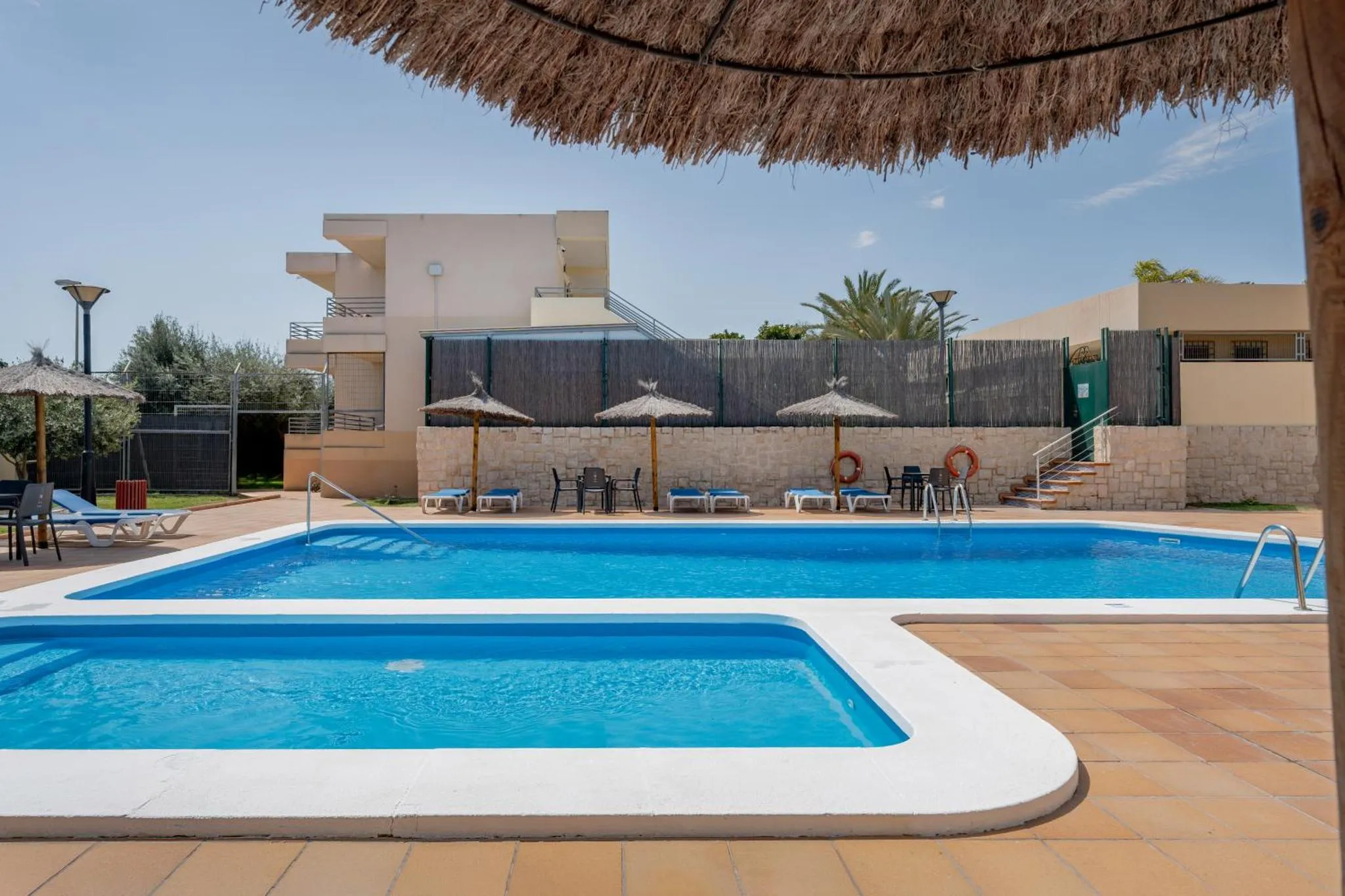 Piscine rectangulaire entourée d'une terrasse carrelée avec des transats et des parasols.
