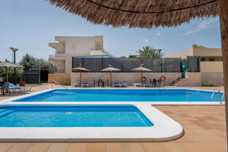 Piscine rectangulaire entourée d'une terrasse carrelée avec des transats et des parasols.