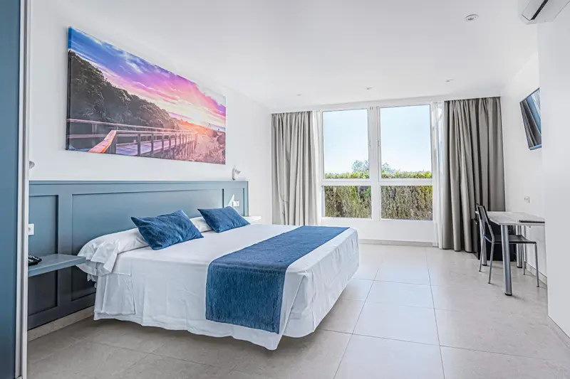 Chambre lumineuse avec un grand lit et une vue sur la végétation.