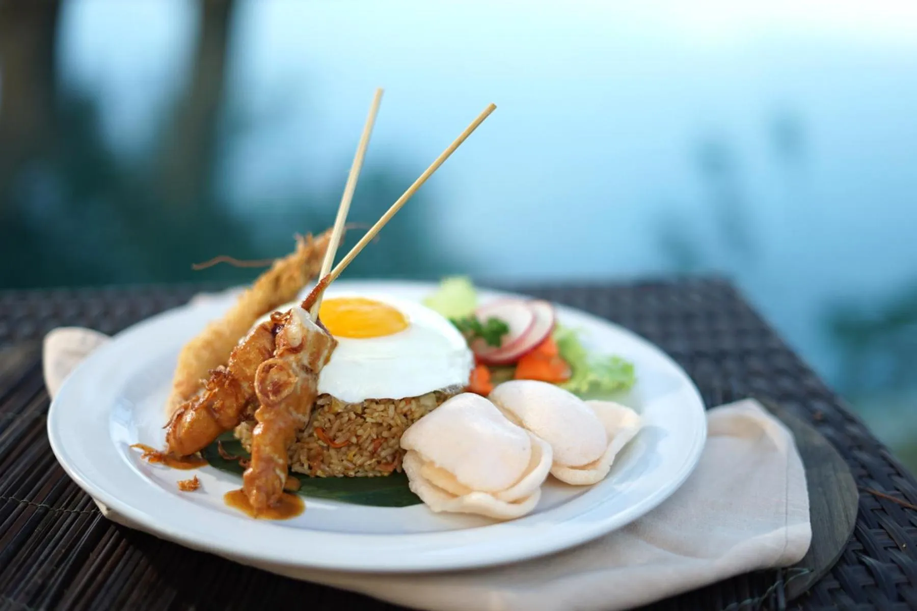 Assiette de riz frit, d'œufs et de brochettes de crevettes sur une table sombre.
