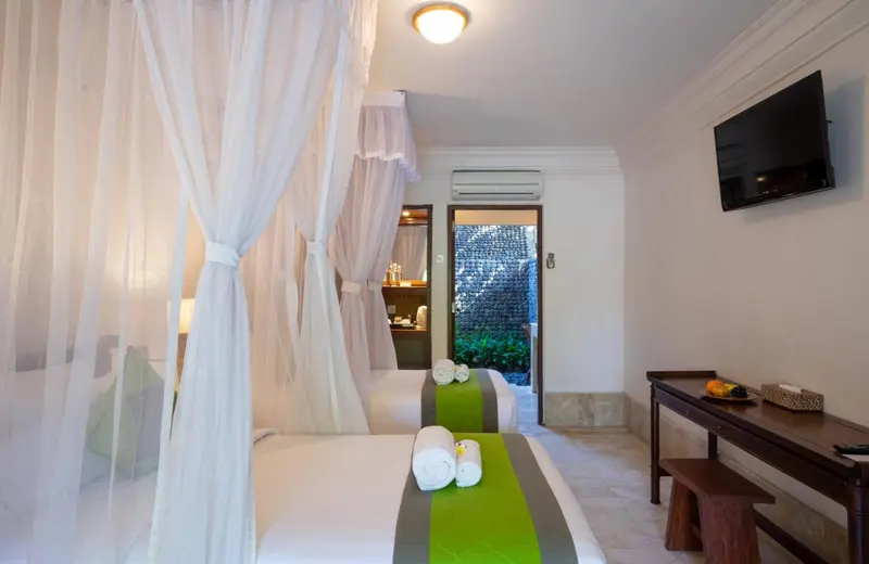 Chambre lumineuse avec deux lits simples et moustiquaire.