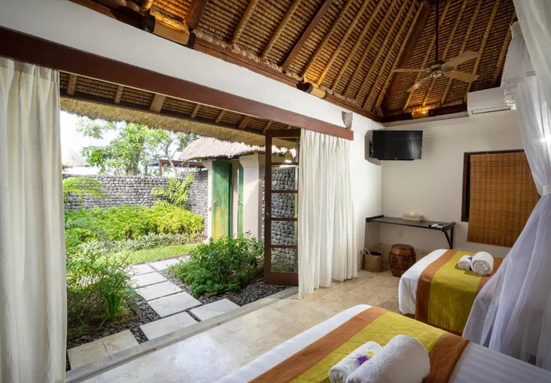 Chambre lumineuse avec deux lits et vue sur un jardin tropical.