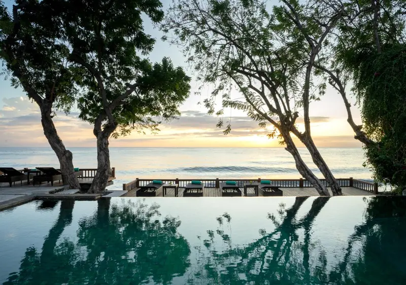 Une piscine à débordement surplombe la mer au coucher du soleil.